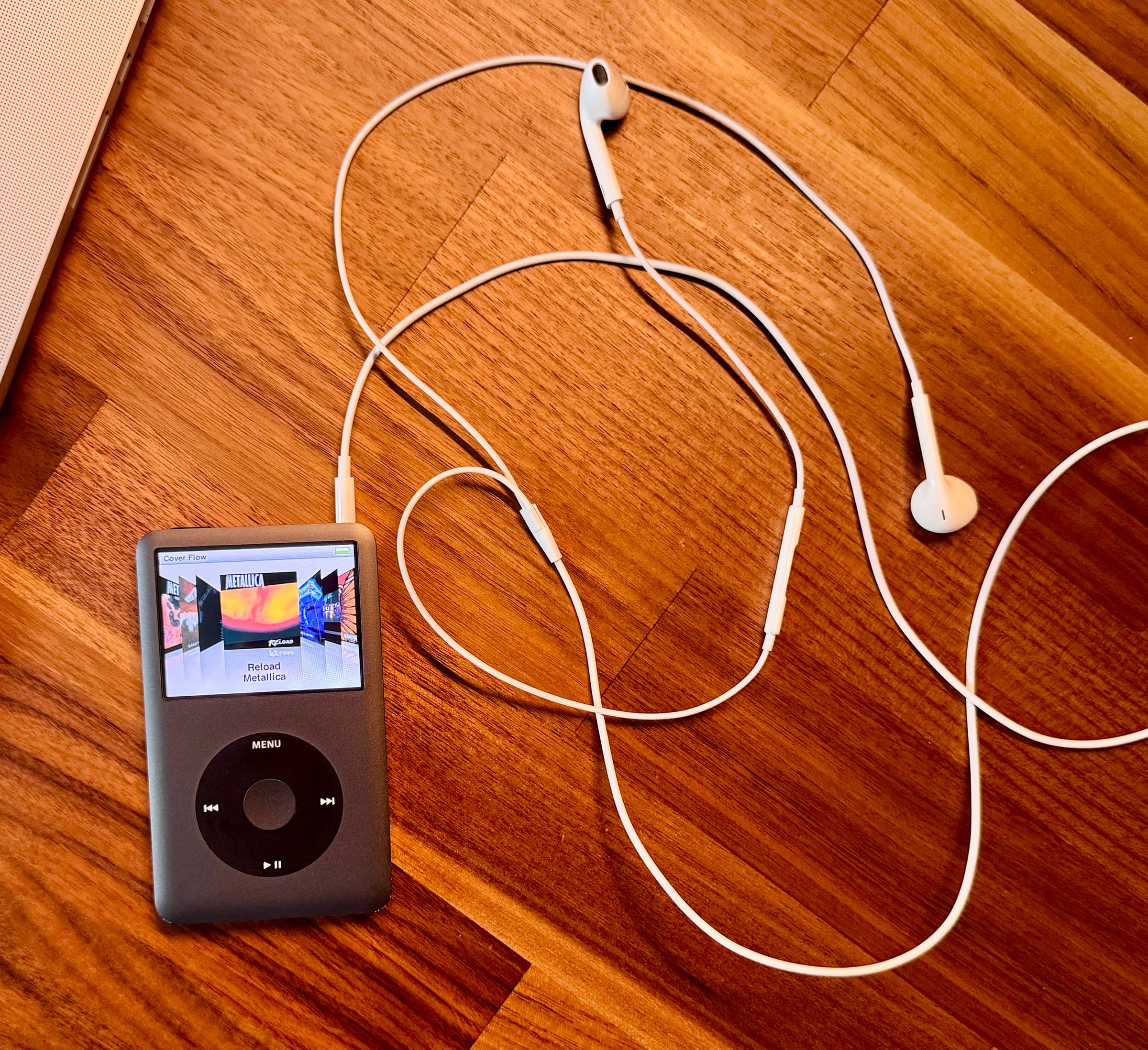 iPod classic с наушниками на деревянном столе, на экране обложка альбома Metallica