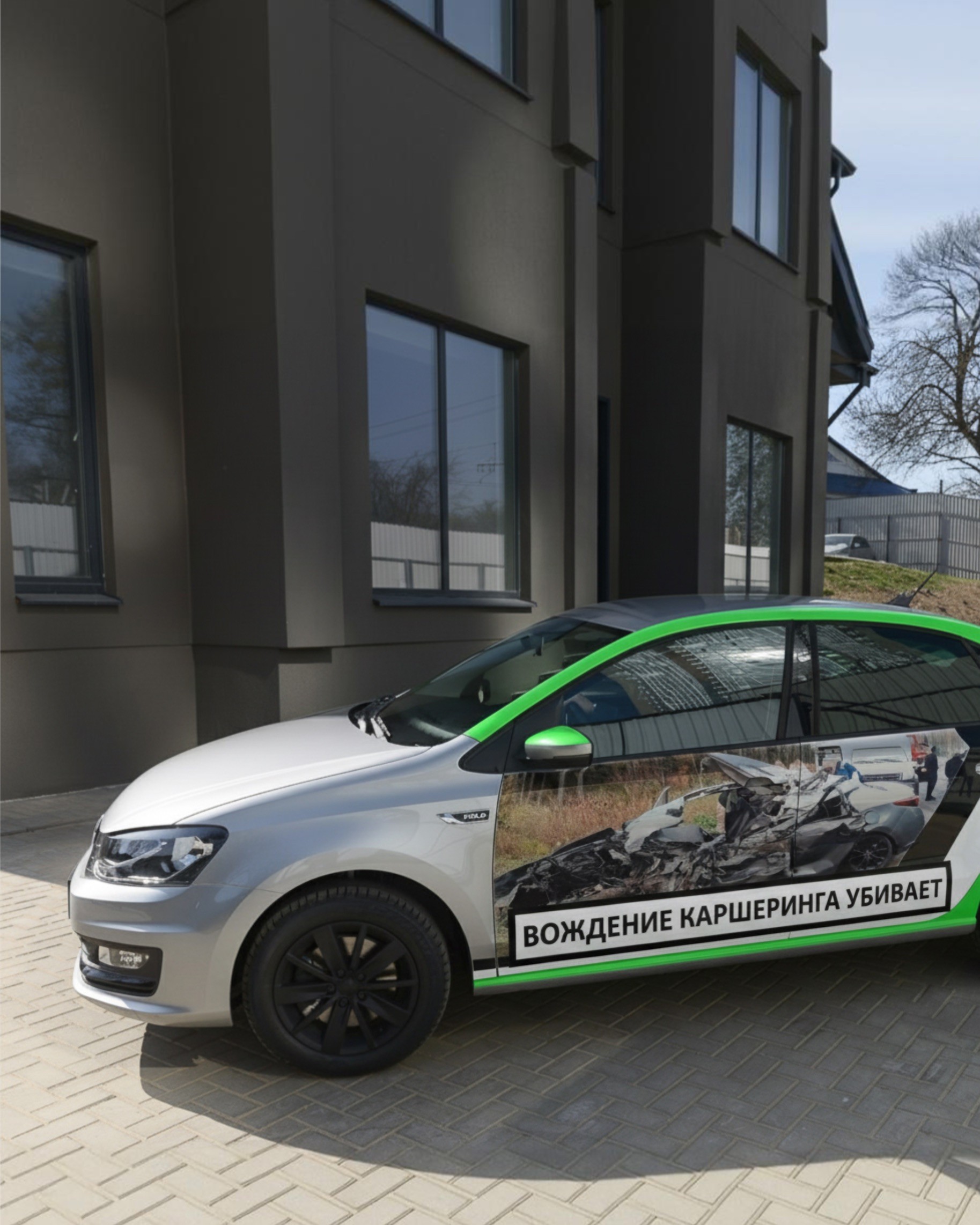 Silver car with green accents and black wheels, parked in front of a modern building. Anti-smoking ad on the side.